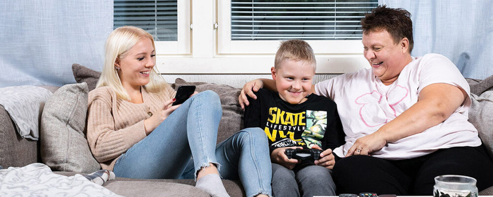 Kaksi aikuista ja kolme lasta istuu lähekkäin sohvalla ja hymyilee.