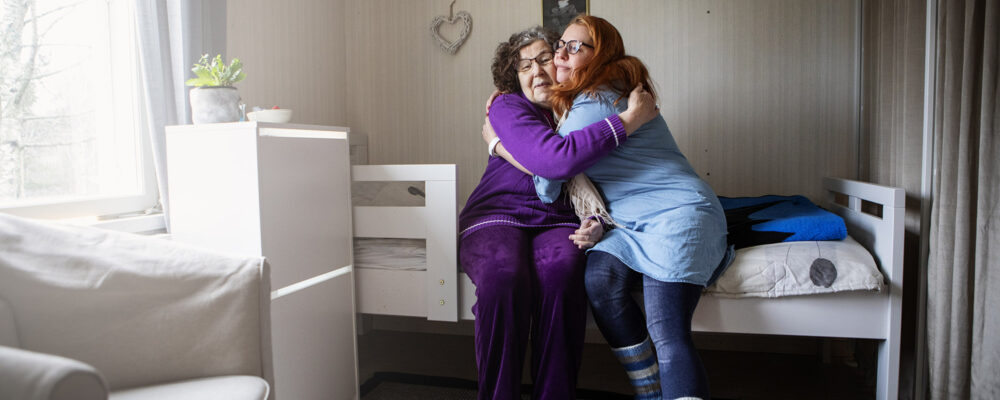Kaksi naista halaa toisiaan sängyn reunalla.
