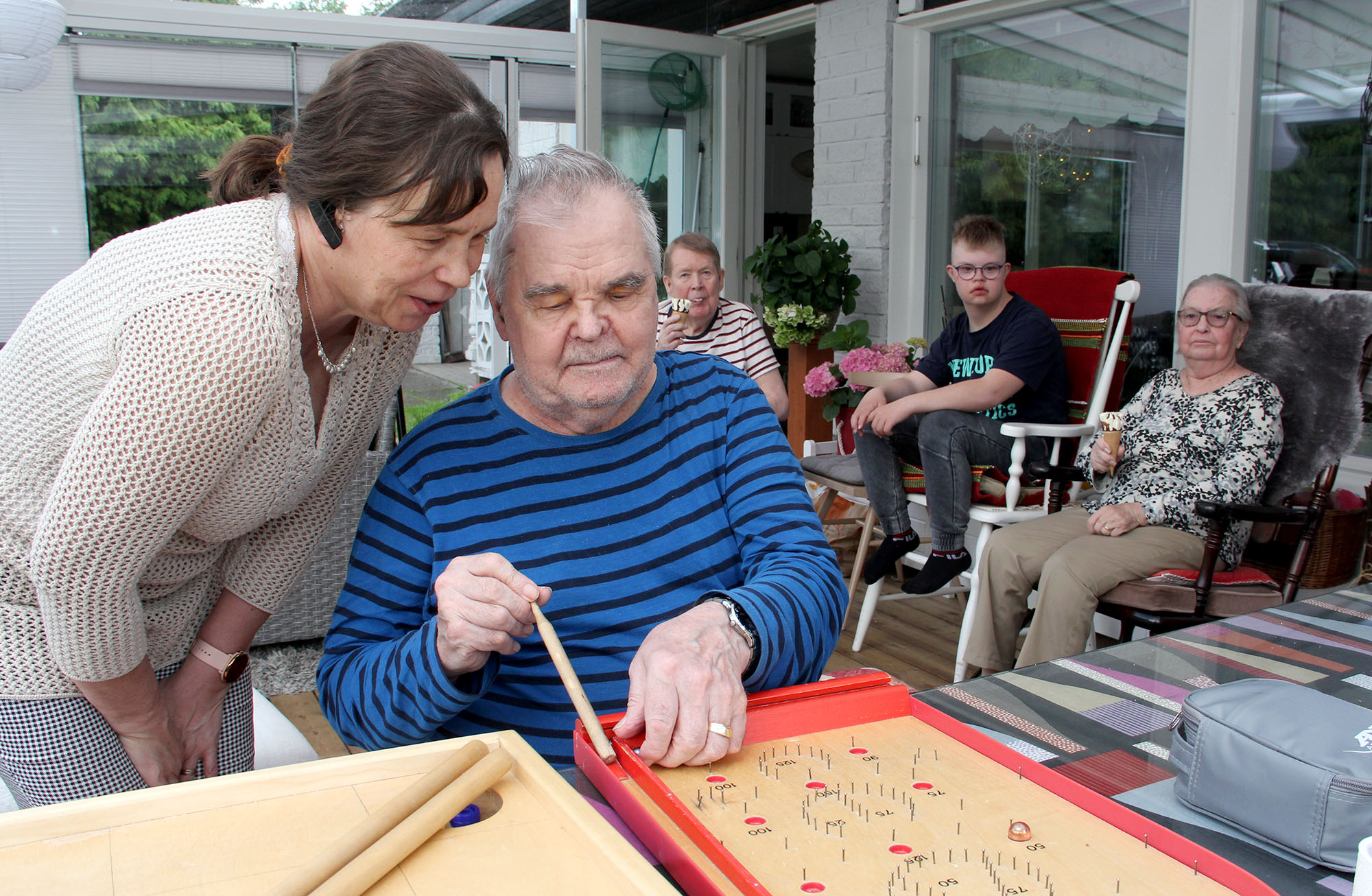 Mies ja nainen pelaavat fortuna peliä talon kuistilla. Takana näkyy myös muita ihmisiä.