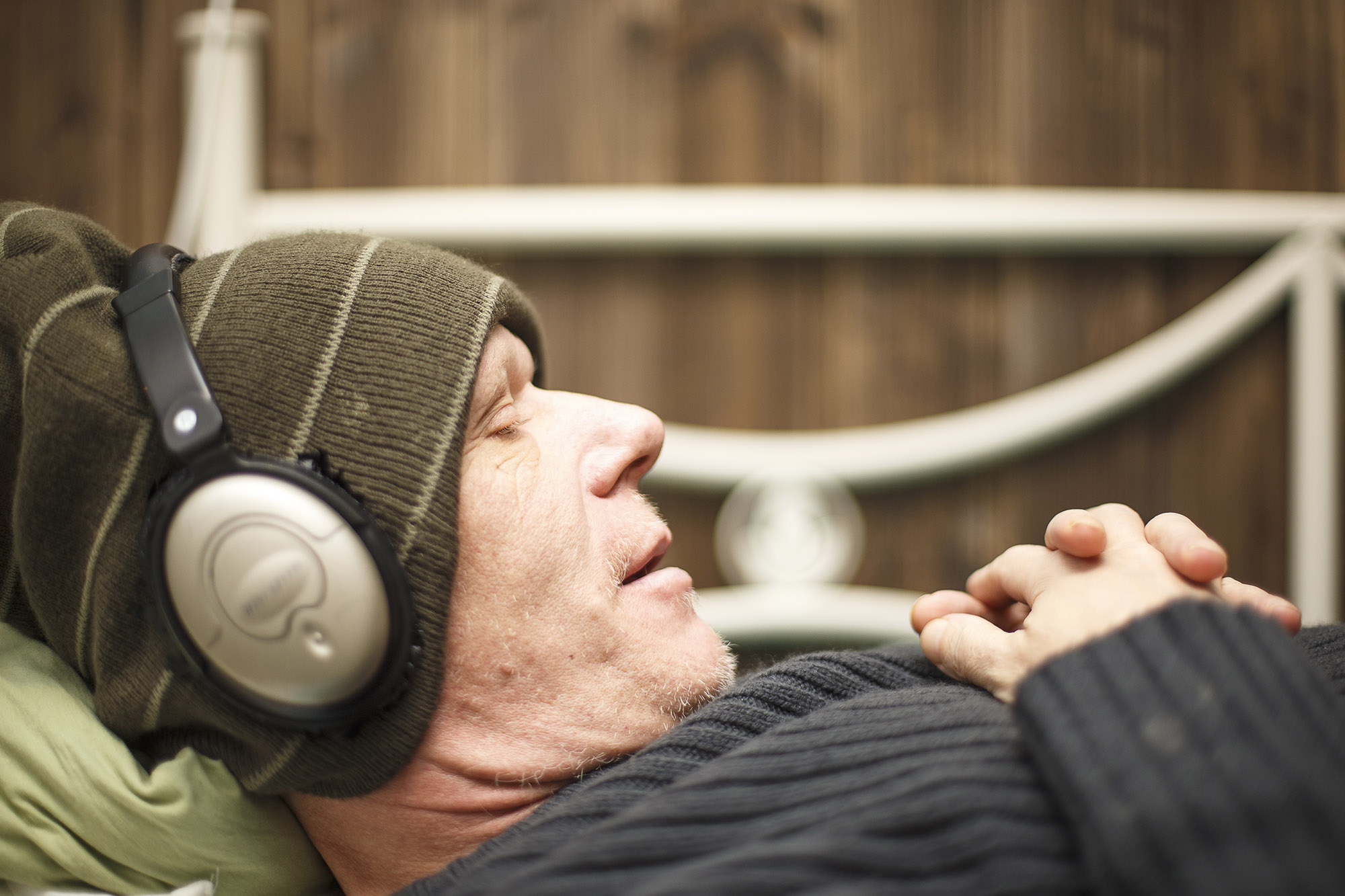 Pipopäinen mies makoilee sängyllä ja kuuntelee musiikkia kuulokkeilla.