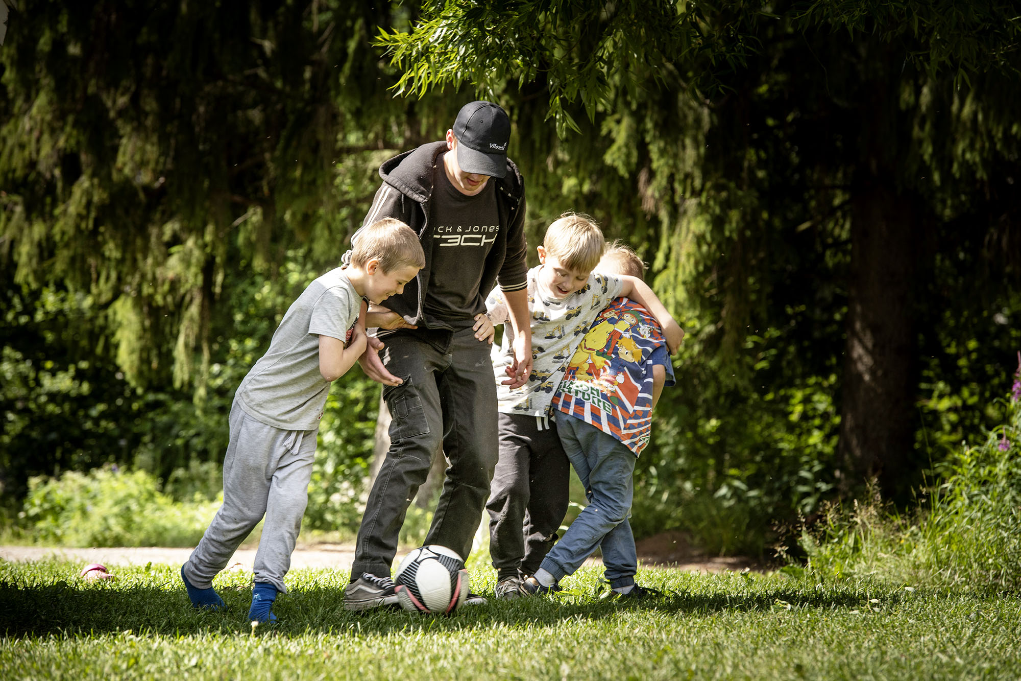 Mies ja kolme poikaa pelaavat jalkapalloa nurmikolla.