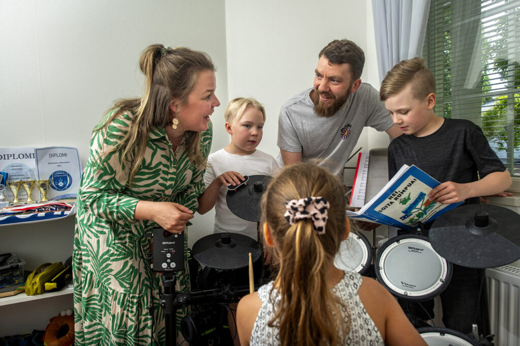 Vanhemmat ja kolme lasta istuvat lasten rumpusetin äärellä musisoimassa.