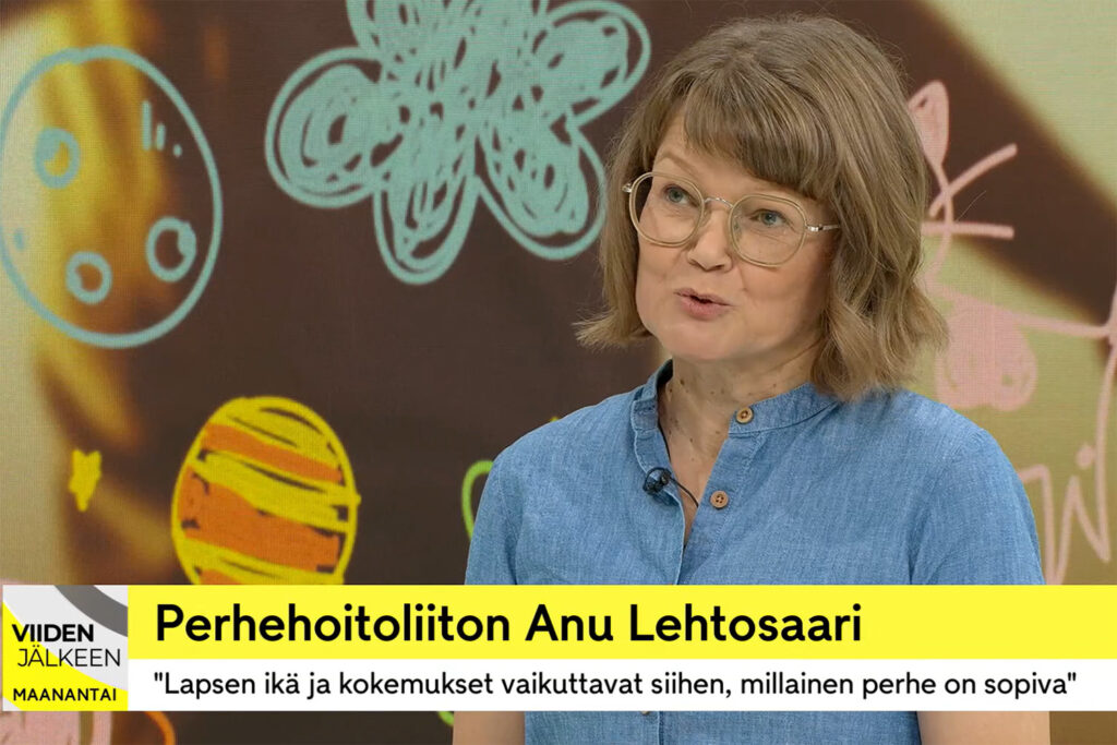 Nainen puhuu tv-studiolla, taustalla piirroskuvia