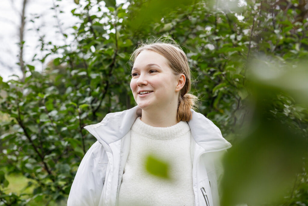 Nuori nainen hymyilee lehtipuiden katveessa.