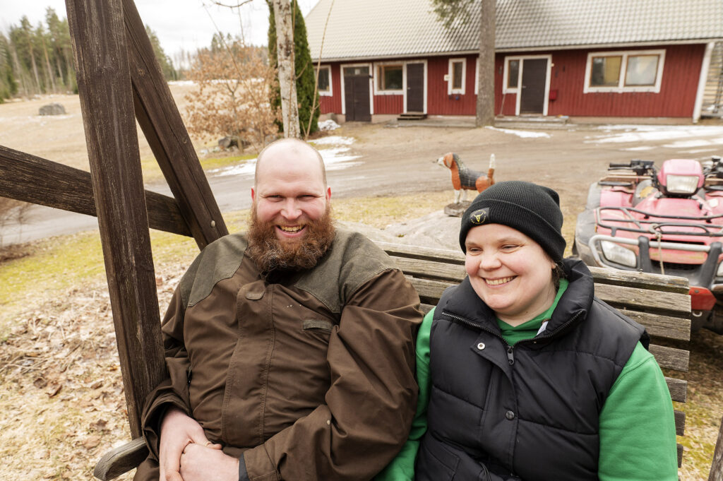 Mies ja nainen istuvat vierekkäin pihakeinussa ja hymyilevät.