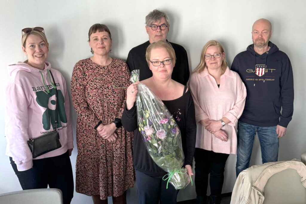 Joukko ihmisiä seisoo rivissä, yhdellä on käsissään kukkapaketti .