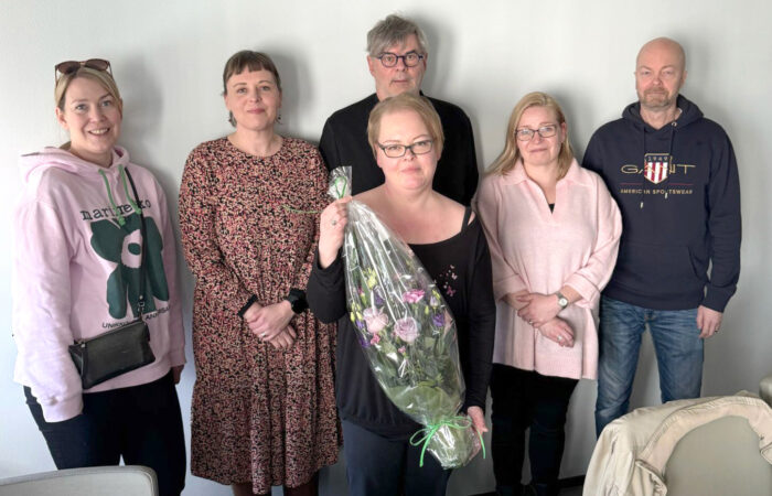 Joukko ihmisiä seisoo rivissä, yhdellä on käsissään kukkapaketti .