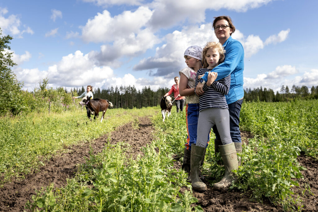 Aikuinen halaa kahta lasta kesäisellä pellolla.