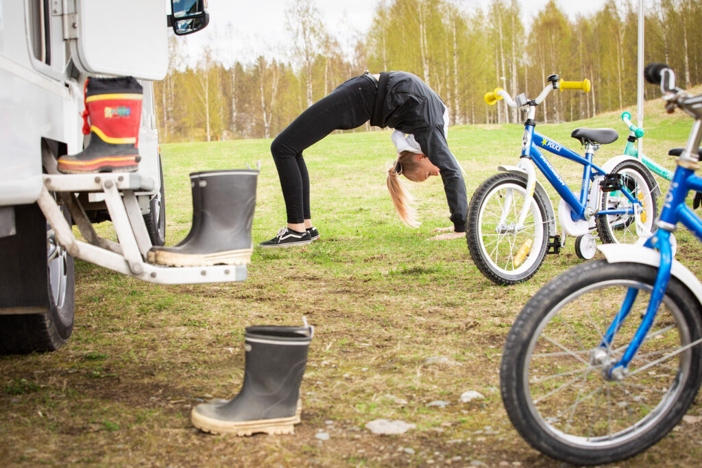 Tyttö voimistelee nurmikolla asuntoauton ja polkupyörien vieressä.