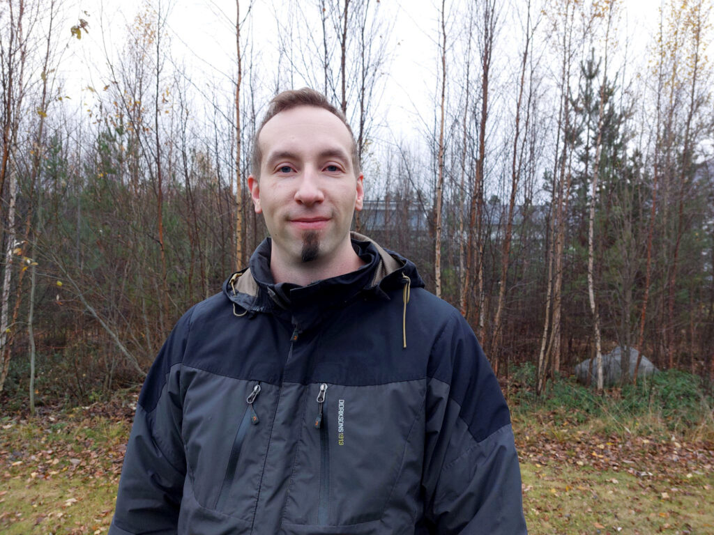 Mies seisoo ulkona taustallaan lehdettömiä koivuja.