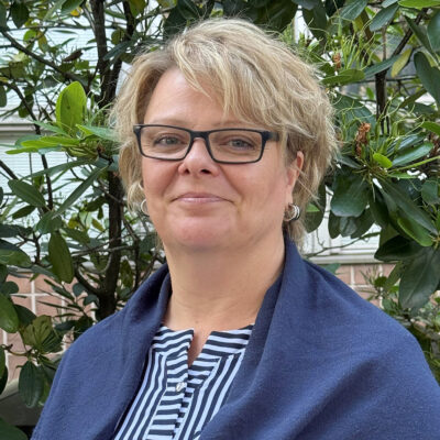 Sinipaitainen nainen taustallaan lehtipuu.