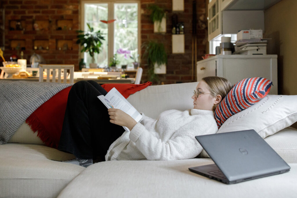Nuori nainen makaa sohvalla ja lukee koulukirjaa.