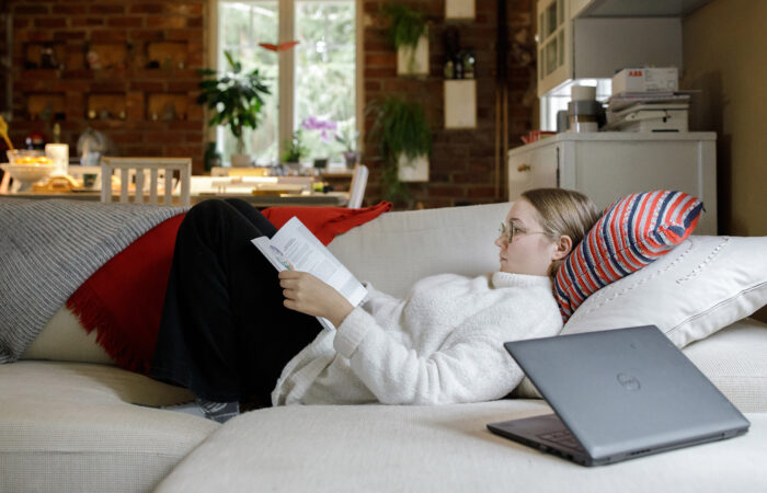 Nuori nainen makaa sohvalla ja lukee koulukirjaa.