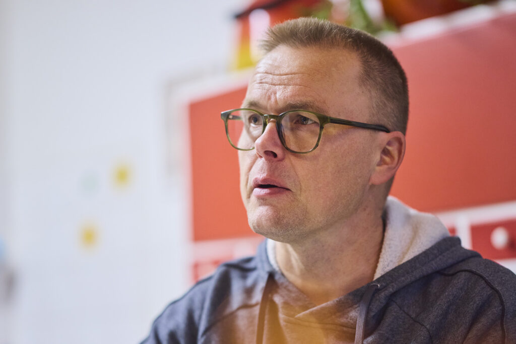 Silmälasipäinen mies keittiössä taustallaan punertava kaappi.