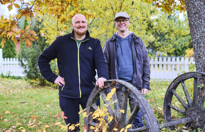 Kaksi miestä seisoo syksyisellä pihalla edessään vanhat kärrynpyörät.