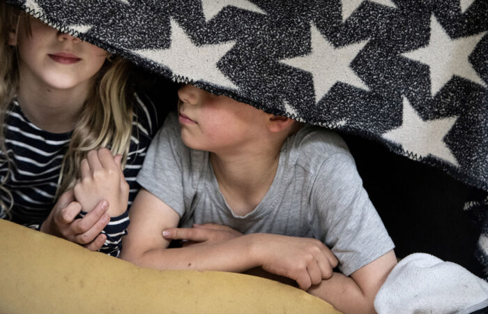 Kaksi lasta makaa sängyllä peitto silmiensä edessä.