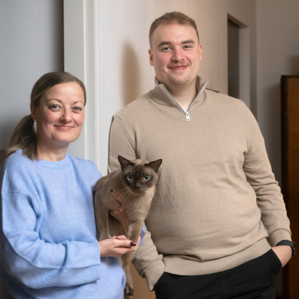 Nainen ja mies hymyilevät, naisella on kissa sylissään.