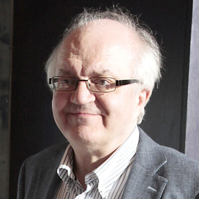 Harmaahiuksinen mies, jolla on silmälasit.