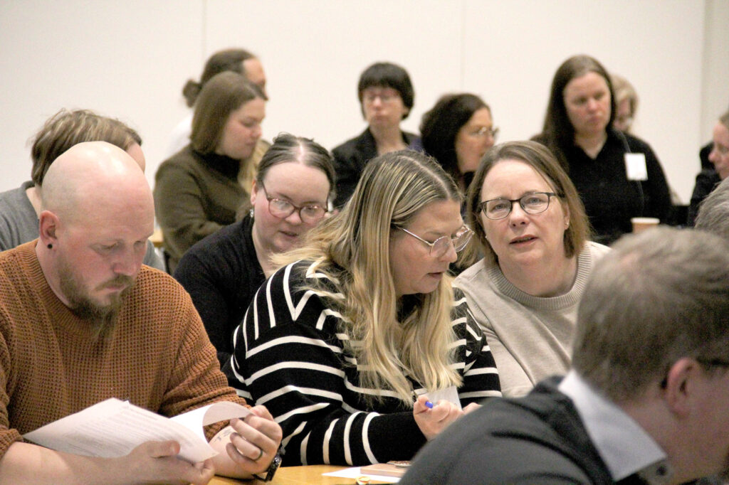 Joukko ihmisiä istuu salissa odottamassa kokouksen alkua.