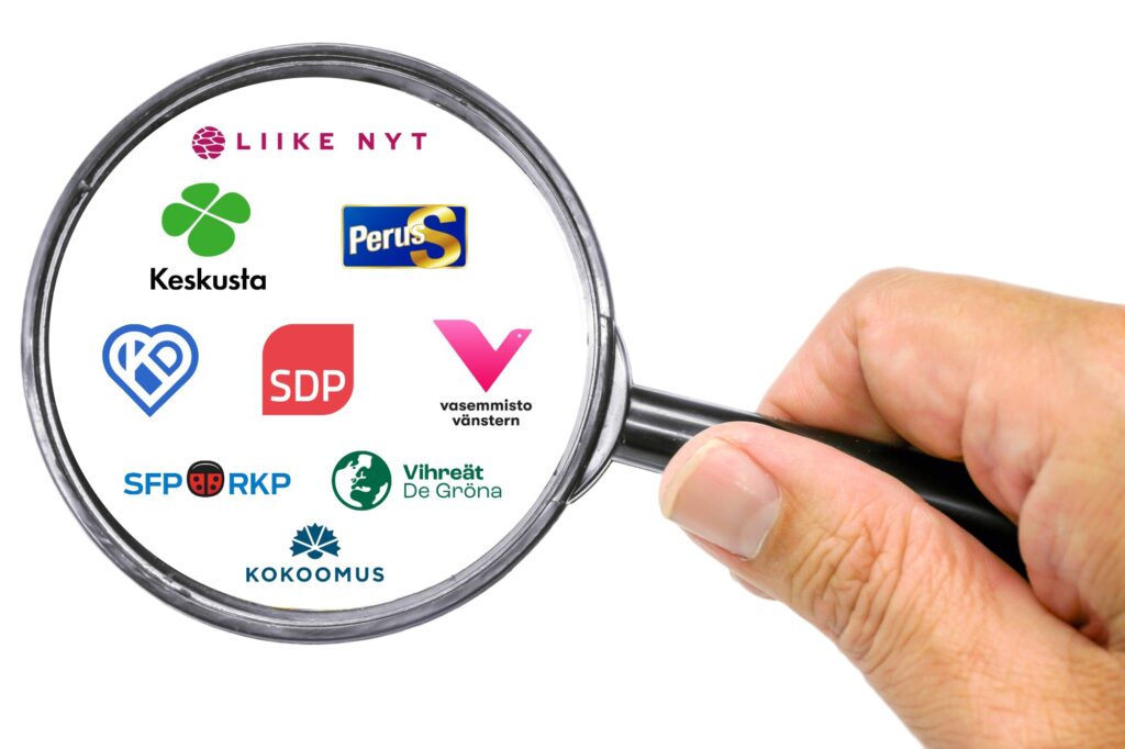 Käsi pitelee suurennuslasia, jonka alla näkyy eduskuntapuolueiden logoja